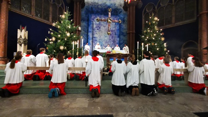 Kirchenchor singt vor Weihnachtsbäumen und Altar.