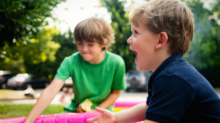 Zwei Jungen spielen im Garten mit einem pinken Schlauch.