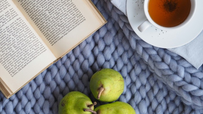 Ein Buch, eine Tasse Tee und drei grüne Äpfel auf einer blauen Decke