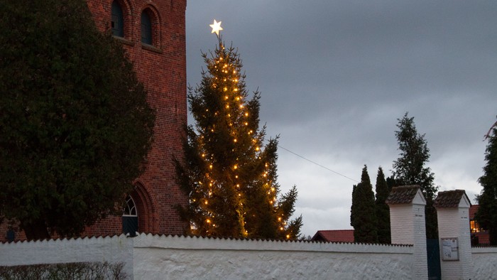En juletree med lys og stjerne foran røde murstensbygning.