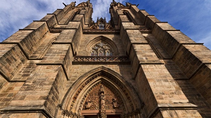 Gotische Kathedralenfassade mit aufwendigen Schnitzereien und Statuen unter blauem Himmel.