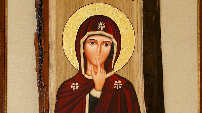 Das Bild zeigt eine religiöse Ikone einer Frau in rotem Gewand mit goldenem Heiligenschein.