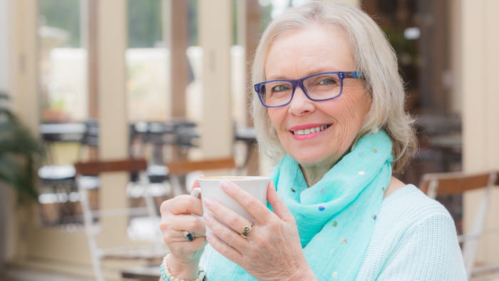 Eine ältere Frau trinkt in einem Café eine Tasse Kaffee.