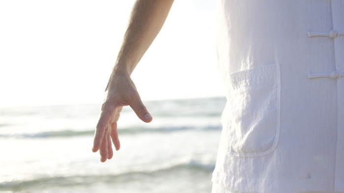 Eine Person am Strand mit ausgestrecktem Arm, Sonnenlicht im Hintergrund