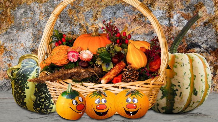 Ein Korb gefüllt mit Herbstgemüse und Blumen, umgeben von Kürbissen mit Gesichtern