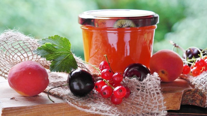 Ein Glas mit Früchten und eine Holzplatte mit verschiedenen Beeren und Blättern