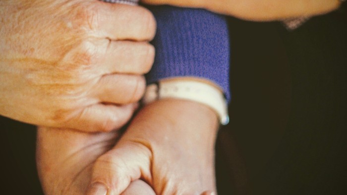 Eine ältere Person, die die Hand eines Kindes hält.