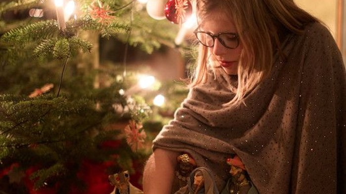 Ein Mädchen spielt mit einer Krippe vor einem Weihnachtsbaum.