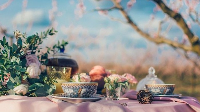 Ein Tisch mit Teekanne, Tassen und Blumen im Freien unter blühenden Bäumen