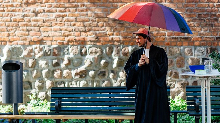 Oskar Hoffmann im Talar mit Regenbogenschirm vor Kirche