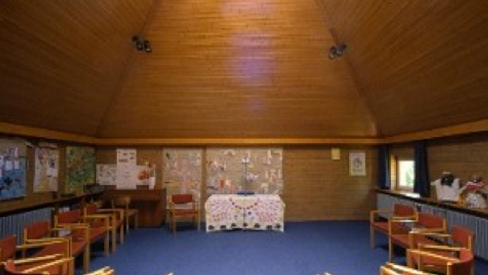 Ein großer Raum mit Holzwänden und blauen Teppichboden, mehrere Stühle und Tische, ein Tisch mit Tischdecke in der Mitte