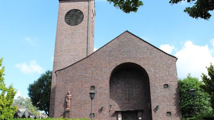 Das Bild zeigt eine Ziegelkirche mit hohem Turm und Rundbogenfenster.
