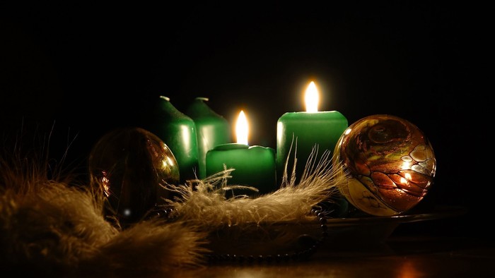 Dunkle Szene mit brennenden grünen Kerzen und goldenen Christbaumkugeln