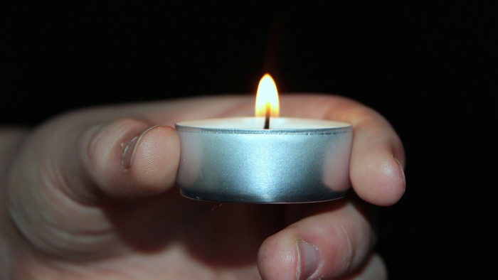 Eine Hand hält eine brennende Teelichtkerze.