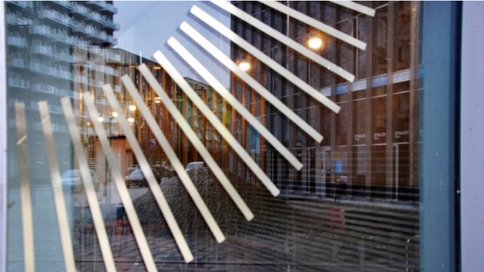 Moderne bygning med reflekterende glasvinduer, der afspejler gadelygter og nærliggende bygninger.