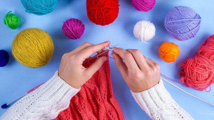 En person spinder med røde tråde, omgivet af mange boller med farvede garn.