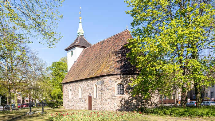 Kleine Kirche mit spitzem Turm in parkähnlichem Gebiet