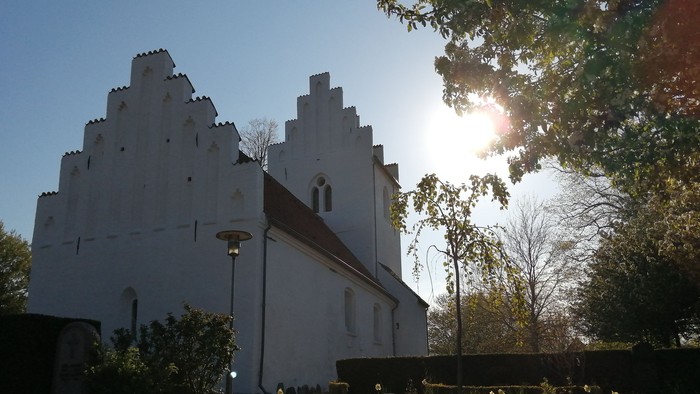 Et hvidt historisk kirkebygningskompleks med en sollysende gennem træerne