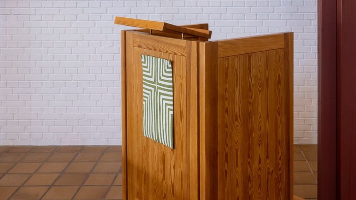 En træpult i kirke med korset på forside og en liste med tal på bagside