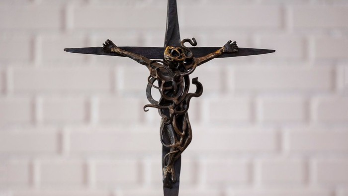 En smedejernskulptur af Jesus Kristus på korset står på en hvid flise.