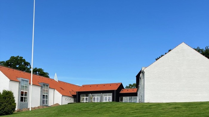 En hvid bygning med røde tag og en flagstang foran