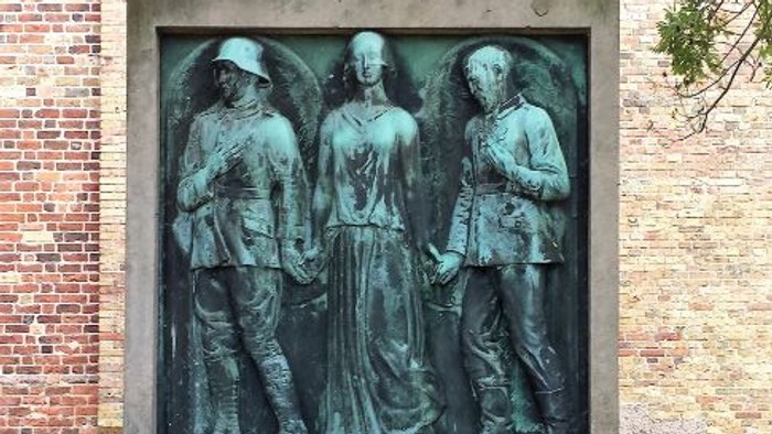 Støvletøg med tre figurer foran murstengevær