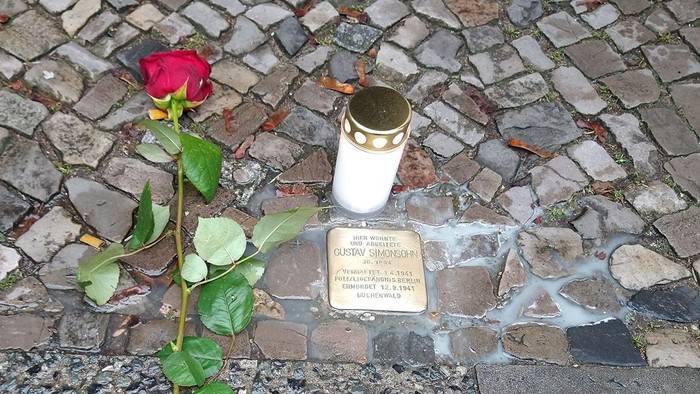 Eine rote Rose und eine weiße Kerze auf einem Kopfsteinpflaster mit einer Gedenktafel