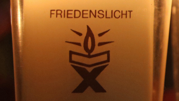 Eine Kerze mit dem Aufkleber *„Friedenslicht Bethlehem“* brennt.