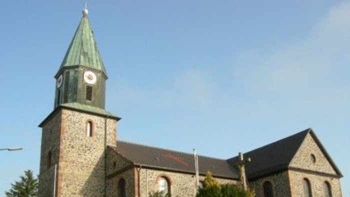 Steinkirche mit hohem Uhrturm und grünem Spitzturm vor klarem blauem Himmel.