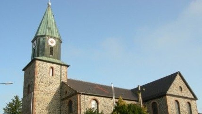 Steinkirche mit hohem Uhrturm und grünem Spitzturm vor klarem blauem Himmel.