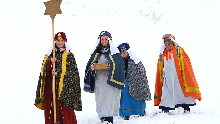 Drei Könige in farbenfrohen Gewändern stehen im Schnee, einer hält einen Stern.