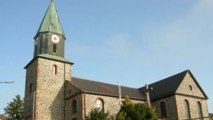 Steinkirche mit hohem Uhrturm und grünem Spitzturm vor klarem blauem Himmel.
