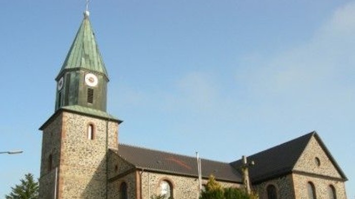 Steinkirche mit hohem Uhrturm und grünem Spitzturm vor klarem blauem Himmel.