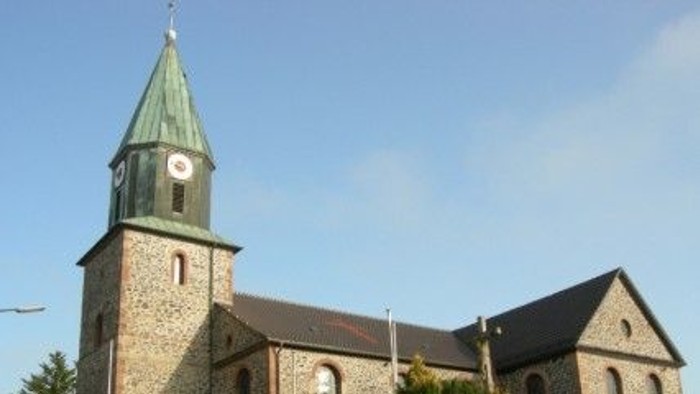 Steinkirche mit hohem Uhrturm und grünem Spitzturm vor klarem blauem Himmel.