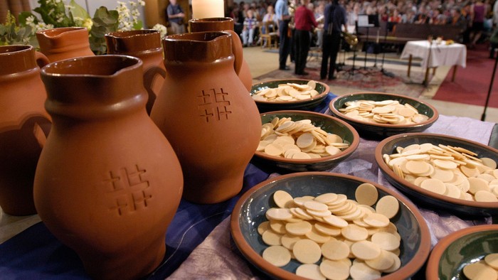 Auf dem Tisch stehen Töpfergefäße und Schalen mit Brezeln, im Hintergrund Menschen.