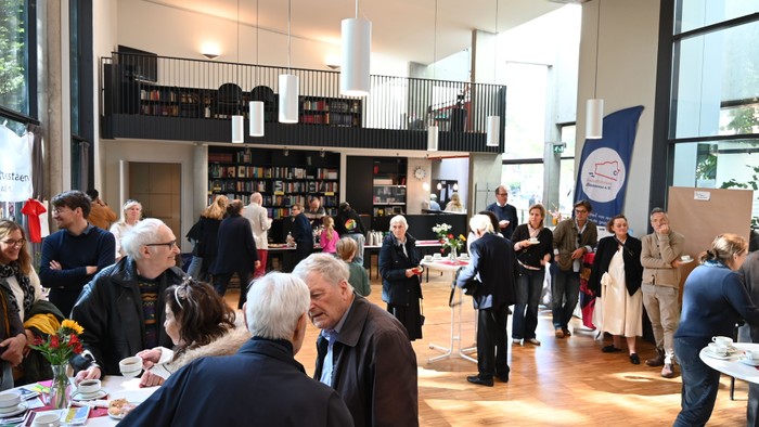 Gesellschaftliches Beisammensein mit Menschen, die sich in einem geräumigen Innenraum mit Bücherregalen und Tischen unterhalten.