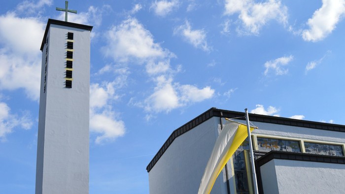 Moderne Kirche mit hohem Glockenturm und geschwungenem Eingangsüberdach unter einem strahlend blauen Himmel.
