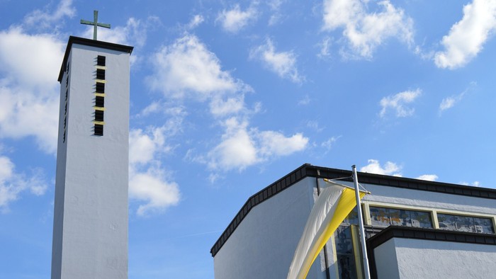 Moderne Kirche mit hohem Glockenturm und geschwungenem Eingangsüberdach unter einem strahlend blauen Himmel.