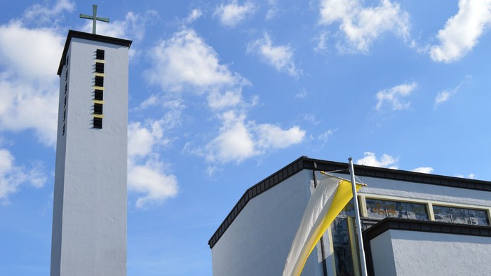 Moderne Kirche mit hohem Glockenturm und geschwungenem Eingangsüberdach unter einem strahlend blauen Himmel.