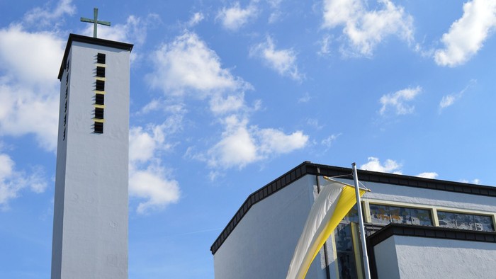 Moderne Kirche mit hohem Glockenturm und geschwungenem Eingangsüberdach unter einem strahlend blauen Himmel.