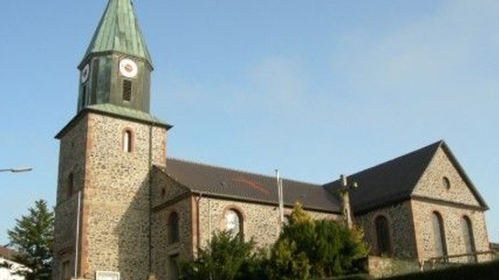 Steinkirche mit hohem Uhrturm und grünem Spitzturm vor klarem blauem Himmel.