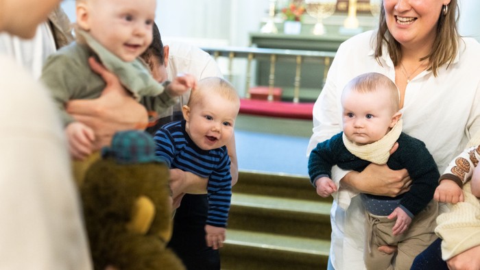 En gruppe af voksne og små børn spiller i et rum med trappe.