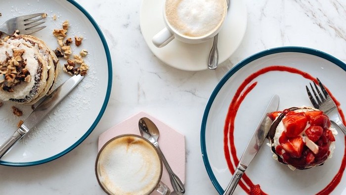 Drei Tassen Kaffee und zwei Teller mit Desserts auf Marmorplatte