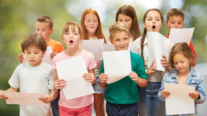 Singende Kinder im Grundschulalter mit Notenblättern in der Hand