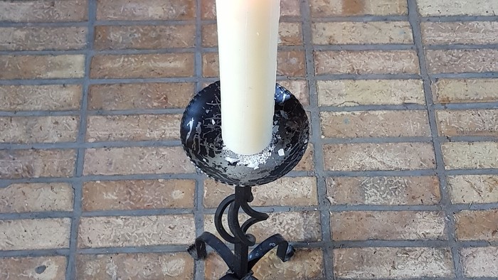 Eine Kerze steht auf einem Ziegelboden in einem Halter.