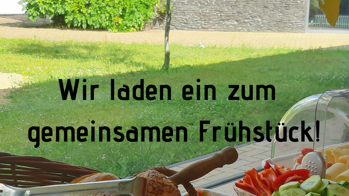 Ein Tisch mit verschiedenen Broten und Gemüsestücken, im Hintergrund ein Baum und ein Gebäude