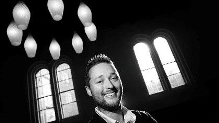 En smilende mand i sort og hvid fotografi foran vinduer og lygter