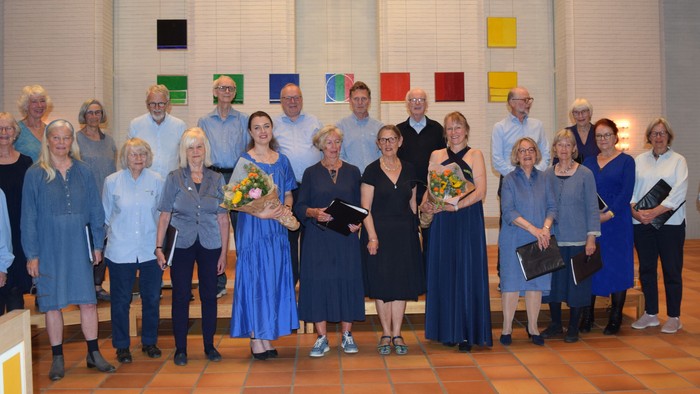 En gruppe korsangere i koordineret påklædning, der holder noder og blomster, og poser formelt sammen.