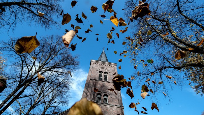 Herbstblätter fallen vor einem Kirchturm vom klaren blauen Himmel