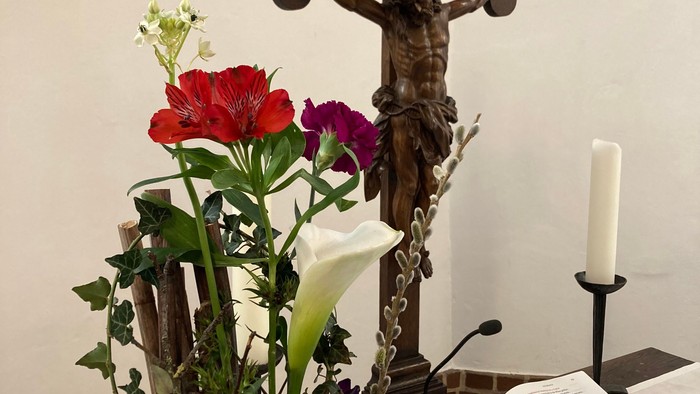 Ein Kreuz mit Jesusfigur, ein Blumenstrauß und eine aufgeschlagene Bibel